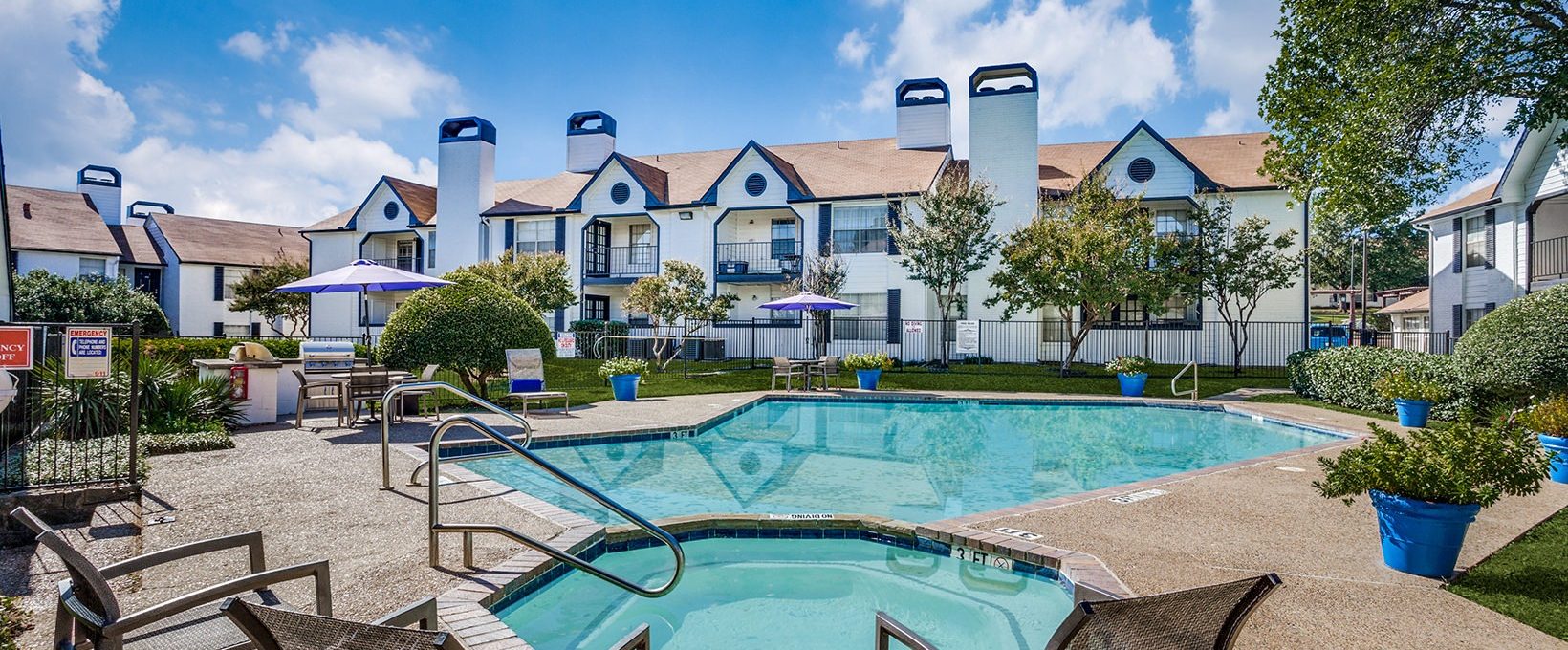 Pool and Hot Tub surrounde by green area and seating, as well as a grill under a parasol